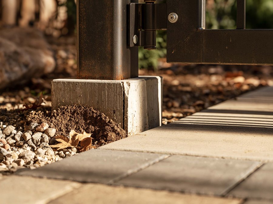 The bottom of a gate post where it goes into the dirt beside a walkway